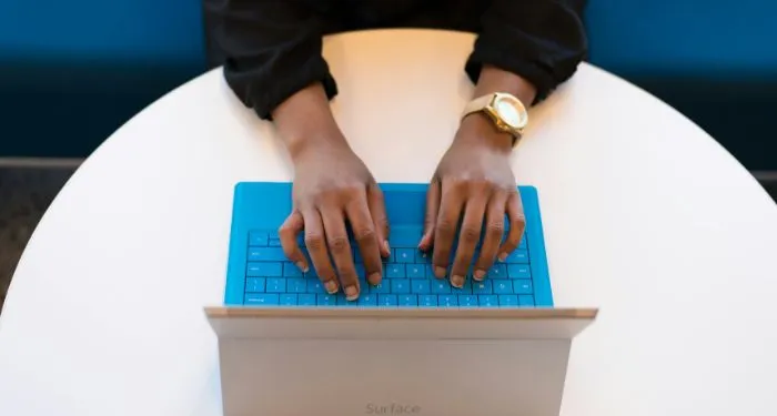 brown-skinned-hands-with-gold-wrist-watch-tying-on-a-blue-keyboard.jpg.webp.webp